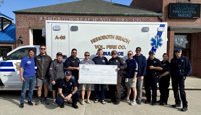 At the check ceremony March 22 are in back (l-r) Mac Payne, The Starboard; Travis Barker, The Starboard; Warren Jones, Rehoboth Beach Volunteer Fire Company vice president; Don Mitchell, Rehoboth Beach Volunteer Fire Company chief engineer; Keith “Toastie” Kirk, The Starboard; Steve “Monty” Montgomery, The Starboard; Chuck Snyder, Rehoboth Beach Volunteer Fire Company fire chief; Doug Moore, The Starboard; Justin Kohler, The Starboard; Zach Stevenson, EMT/firefighter; Yulia Strohmeyer, EMT/firefighter; and Joshua David, EMT/firefighter. Kneeling in front is EMT/firefighter Joshua Keil. ELLEN DRISCOLL PHOTO